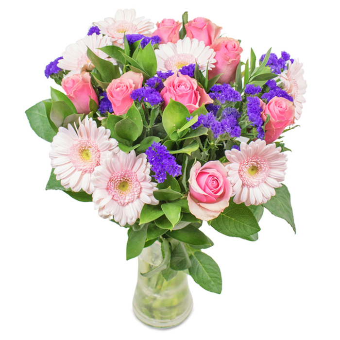 A vibrant, elegantly composed floral bouquet crafted in Chingford and presented in a pristine, transparent glass vase against a clean, white background. Taking center stage are approximately seven to nine roses in shades of soft to medium pink-their signature spirals just beginning to unfold, capturing the anticipation of new beginnings. Interwoven with these are about five to seven pale pink Gerbera daisies, distinguished by broad, radiating petals and light, almost white centers-creating a gentle cloud of colour. Clusters of vivid purple statice bring added depth and a punch of hue, their textural contrast reminiscent of the wildflowers found in Memorial Park. The arrangement sits atop a rich base of deep green foliage, lending volume and freshness that echo the gardens of Chingford Mount. Subtle water reflections shimmer in the clear vase, suggesting a just-arrived delivery ready to brighten a home in Sewardstone or Oak Hill. This bouquet of pink roses, gerberas, and purple accents suits birthdays, anniversaries, Mother's Day, or simply adorning a favorite window-symbolizing joy, connection, and heartfelt celebration within the Chingford community.
