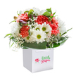 Brimming with light and joyful energy, this bouquet, nestled in a square white gift bag, feels like a pocket of spring gathered just for someone special in Chingford. Peach and coral carnations, their petals ruffled and soft, offer a gentle fragrance and a sense of abundant optimism. Intermixed are snowy white daisies, each sparkling with a lively yellow-green center-the perfect accent for cheering any day, whether in a home near Epping Forest or down Kings Head Hill. A delicate mist of baby's breath meanders throughout, infusing the bouquet with an airy innocence reminiscent of morning walks along River Ching. Hints of unopened, violet-tinged buds peek shyly from the side, promising new beginnings. The polished deep green foliage forms an embracing nest at the base, its glossy leaves grounding the blooms with richness and structure. The bag, finished with neat ribbon handles, signals a mindful, elegant delivery-ready for birthdays, thank-you gifts, or simply to bring delight on an ordinary afternoon. Every flower speaks of expert local hands, careful placement, and a love of sharing beauty in Chingford's close-knit community.