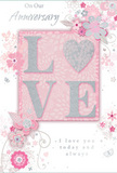 This anniversary card presents a gentle celebration of lasting romance, its design built around the word LOVE, which appears in the centre in soft, raised glitter that gives a slightly embossed, tactile feel under the fingers. The letters shimmer delicately, edged with fine sparkles that echo the silvery tones woven through the rest of the artwork. Instead of a stark white base, the card glows with pastel pinks that deepen just behind the central word, forming a subtle panel that anchors the composition much like the main blooms in a romantic bouquet. Around this focal point, a graceful scattering of stylised flowers in blush, mauve, and whisper-soft grey unfurls across the card, painted in a way that resembles watercolour strokes rather than sharp outlines. Their petals and leaves curve gently, reminiscent of the soft, flowing shapes in arrangements often delivered to homes along Chingford's quiet residential roads and near the bustle of Chingford Mount. Tiny flourishes-swirling lines, minute petals, and a few barely-there butterflies-add movement, giving the impression of a lightly perfumed breeze drifting over an English spring garden. The background remains softly textured in tone rather than pattern, allowing the floral motifs and central text to stand out while still creating an overall sense of harmony. Delicate script wording, including a tender anniversary greeting and a promise of love today and always, appears in understated, graceful lettering that feels heartfelt and true. The card's mood is intimate and reflective, a keepsake that harmonises beautifully with an anniversary bouquet ordered locally for same-day delivery across Chingford and the nearby neighbourhoods.
